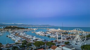 A marina with numerous boats docked, a large Ferris wheel, and a castle in the background.