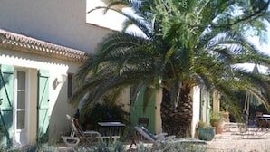 Ein Gebäude mit grünen Fensterläden, einer Palme und Gartenmöbeln.