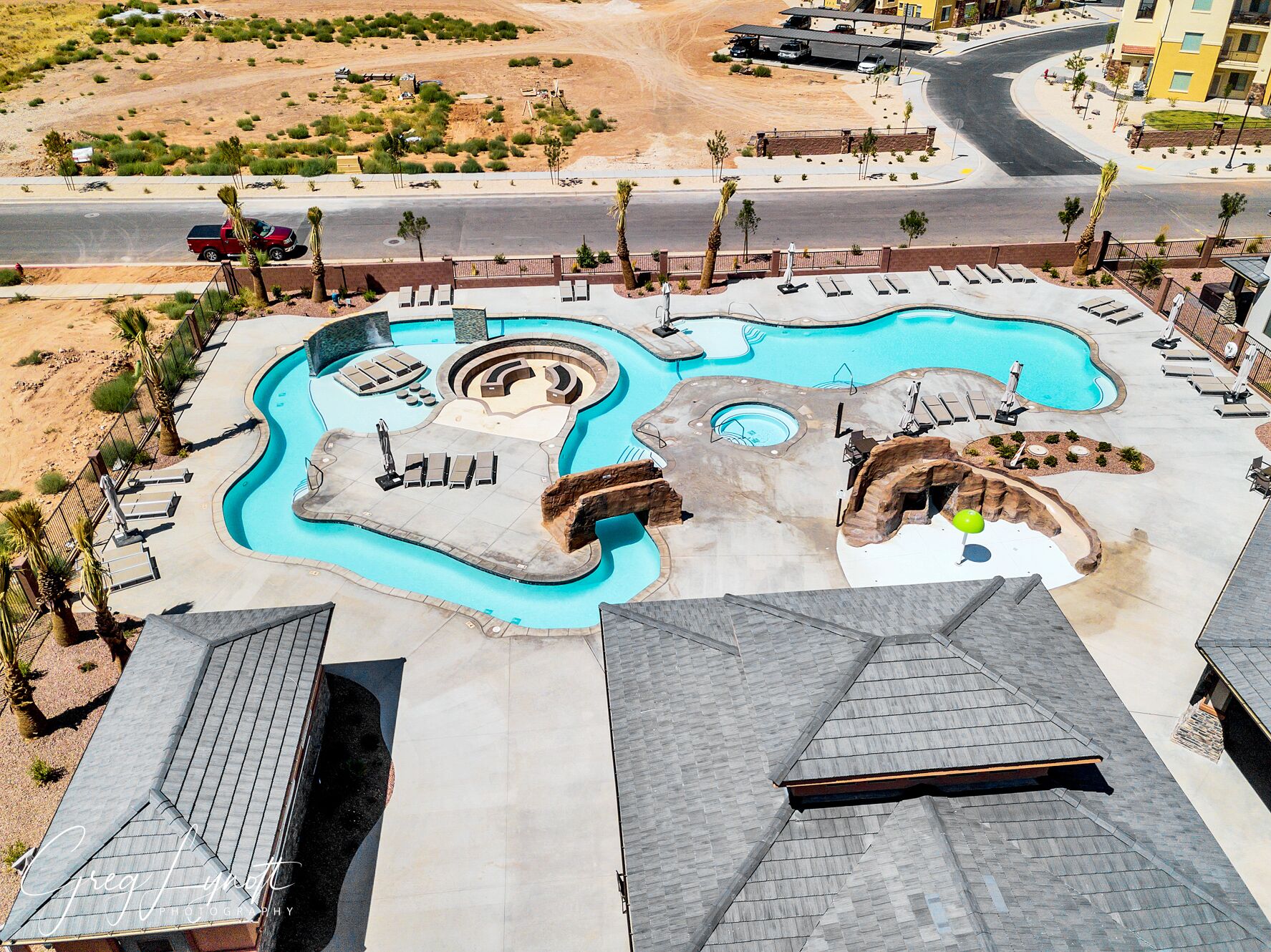 A swimming pool with multiple sections and lounge chairs, surrounded by a landscaped area with palm trees.