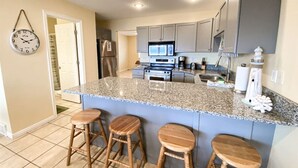 A modern kitchen with granite countertops, a central island with stools, grey cabinets, and a microwave. - Lake View Condo 890 # 2 (Free Wi-Fi) (Garden City)