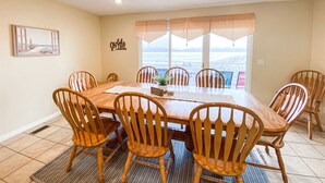 A dining room with a large wooden table and six chairs, a potted plant, and a view of the ocean through large windows. - Lake View Condo 890 # 2 (Free Wi-Fi) (Garden City)