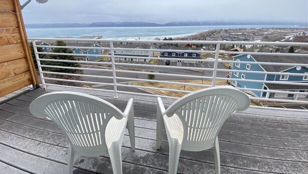 A balcony with two white chairs, a railing, and a view of a coastal town with houses and a body of water. - Lake View Condo 890 # 2 (Free Wi-Fi) (Garden City)