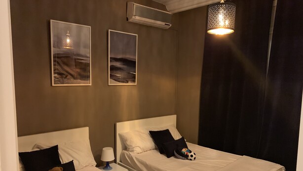Une chambre avec deux lits, un ours en peluche, une lampe et des œuvres d’art accrochées au mur.