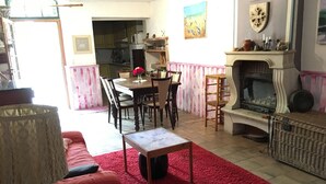 A cozy living room with a red carpet, a fireplace, a dining area with a table and chairs, and a kitchen in the background. - 9-person country house with small spa (Capestang)