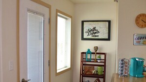 A hallway with a wooden floor, a door with blinds, a small rug, a shelf with decorative items, and a coffee maker on a counter. - Downtown Charmer-2 bed/2 bath (Fargo)