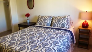 A bedroom with a patterned bedspread, a bedside table with a vase of flowers, a mirror on the wall, and a lamp on a nightstand. - Downtown Charmer-2 bed/2 bath (Fargo)