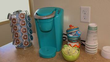 Un comptoir de cuisine avec une machine à café, un support à dosettes de café, un saladier vert et une pile d’assiettes.