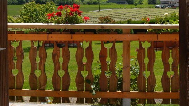 Un balcon doté d’une balustrade en bois, donnant sur un paysage verdoyant avec des champs et des collines lointaines.