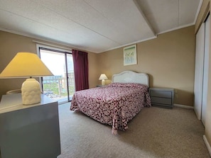 Une chambre d’hôtel avec un lit, un bureau, une lampe, une fenêtre avec des rideaux et un tableau au mur.