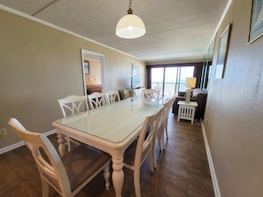 Un espace repas avec une table à plateau en verre, des chaises blanches et un luminaire suspendu.