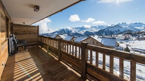 A wooden balcony with a view of snow-covered mountains and a town below. - Modern and warm apartment on the slopes, up to 6 guests (LA TOUSSUIRE)