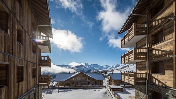 A wooden chalet with a snow-covered roof, a balcony, and a view of snow-capped mountains. - Modern and warm apartment on the slopes, up to 6 guests (LA TOUSSUIRE)
