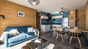 A modern living room with a blue sofa, a glass coffee table, and a dining area with a wooden table and chairs. - Modern and warm apartment on the slopes, up to 6 guests (LA TOUSSUIRE)