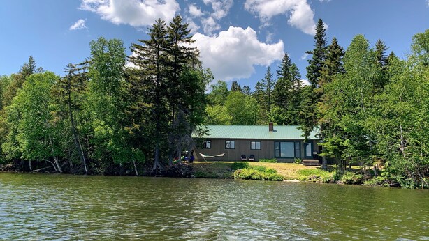 A lakeside cabin with a green roof, surrounded by dense forest and a calm lake. - Rangeley Waterfront Retreat: 4 Bed, 2 Bath, Perfect for Families to Unwind (Rangeley)