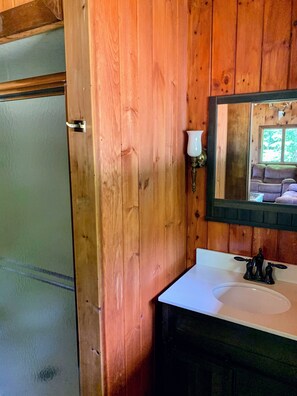 A wooden interior with a white sink, a mirror, and a door. - Rangeley Waterfront Retreat: 4 Bed, 2 Bath, Perfect for Families to Unwind (Rangeley)