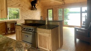 A wooden cabin kitchen with a central island, a stove, and a ceiling fan. - Rangeley Waterfront Retreat: 4 Bed, 2 Bath, Perfect for Families to Unwind (Rangeley)