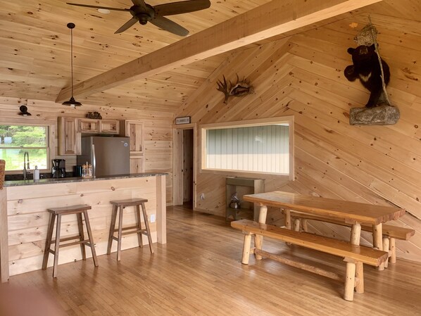 A cabin interior with a kitchen, dining area, and a ceiling fan. - Rangeley Waterfront Retreat: 4 Bed, 2 Bath, Perfect for Families to Unwind (Rangeley)