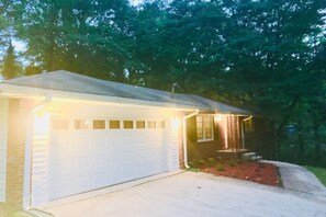 Situated in a wooded area, this home features a garage with a small porch and a light fixture above the entrance.