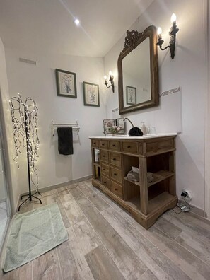 Un baño con tocador de madera, un espejo grande, luces empotradas en la pared y una lámpara de pie.