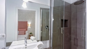 Un baño moderno con ducha de vidrio, un lavabo blanco y un espejo.