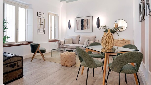 Una sala moderna con una mesa de centro de vidrio, sillas tapizadas en color verde, un sofá y una mesa de comedor.