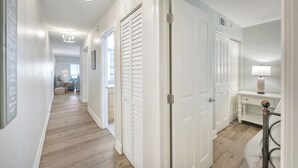 A hallway with wooden flooring, white walls, and a white door. There is a small table with a lamp and a chair in the corner. - Captiva Beach Villas 🏝 On The Gulf Beach (Captiva)