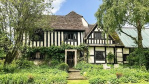 A traditional Tudor-style house with a stone foundation, black and white timber framing, and a steeply pitched roof.