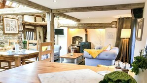 A cozy living room with a stone wall, wooden beams, a blue sofa, and a dining area with a wooden table and chairs.