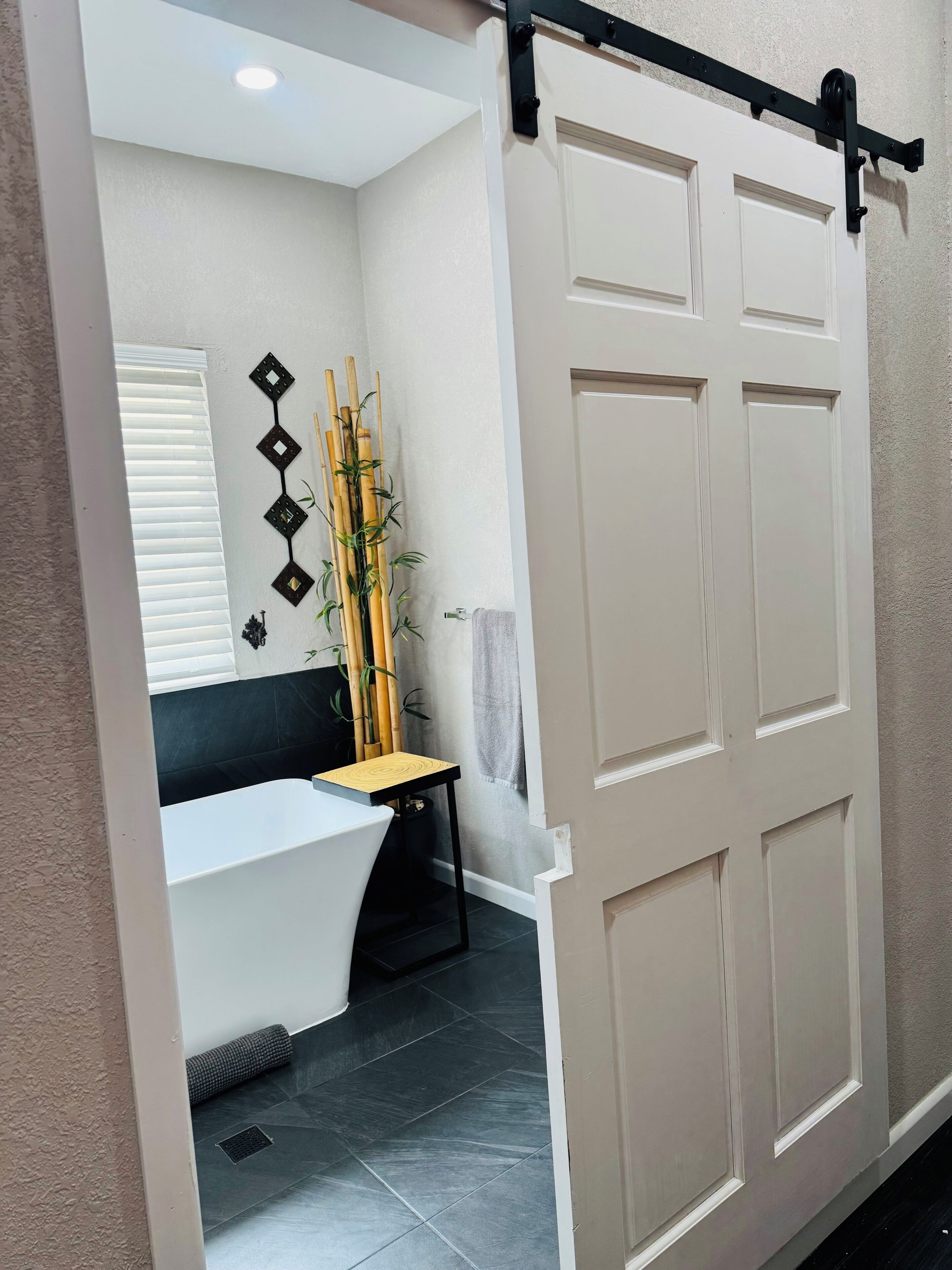 A bathroom with a white bathtub, a bamboo plant, and a towel rack.