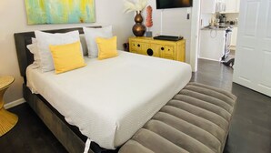 Un dormitorio moderno con una cama grande, televisión y una cocina al fondo.