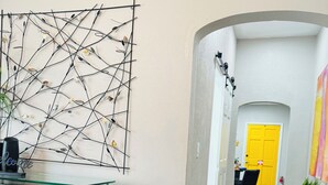 Un pasillo con decoración moderna, que incluye un cuadro de metal negro, una mesa de centro de vidrio y una silla de mimbre.