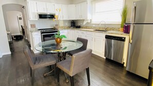 Una cocina moderna con armarios blancos, un refrigerador de acero inoxidable y una zona de comedor con una mesa y sillas de vidrio.