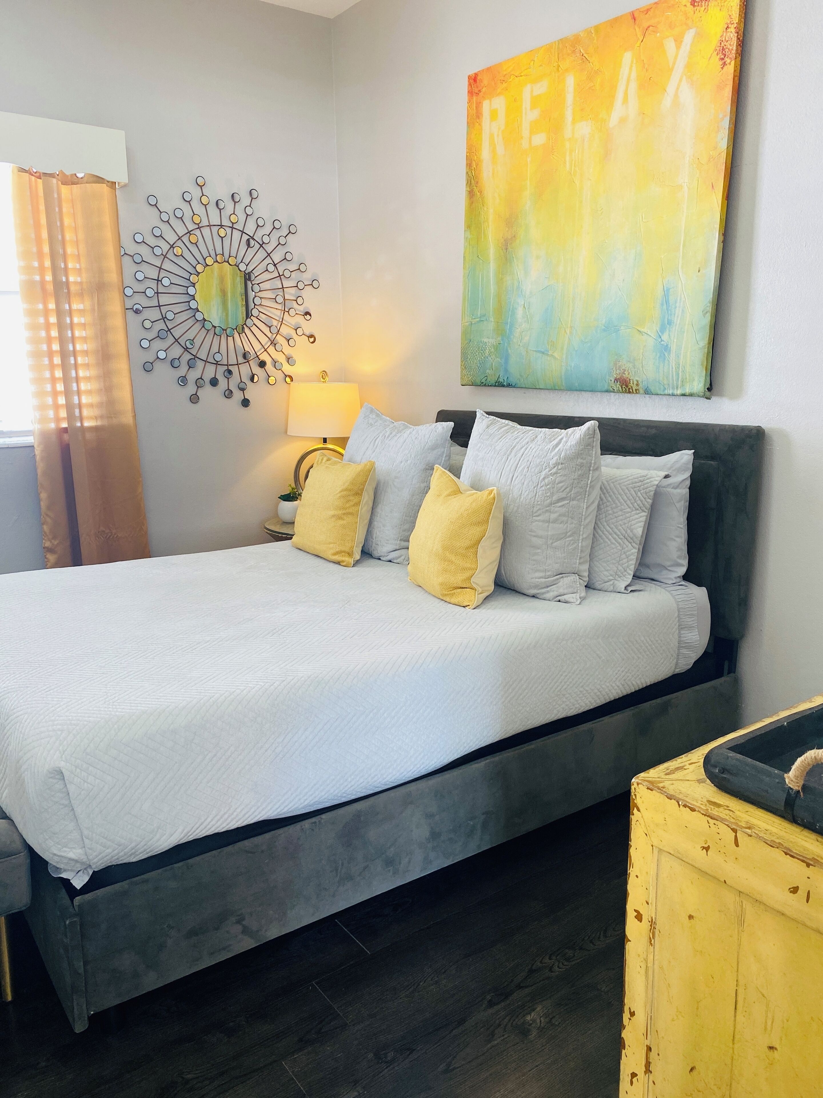 A modern bedroom with a large bed, a wall clock, a painting, and a side table.