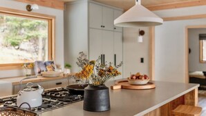 Une cuisine moderne équipée d’une cuisinière à gaz, d’une bouilloire, d’un vase avec des fleurs et d’un saladier de fruits posé sur le comptoir.