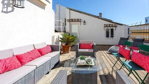 Un patio al aire libre con mobiliario de mimbre, una mesa de centro de vidrio y una planta en maceta.