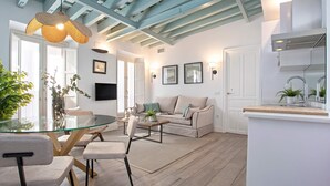 Una sala de estar moderna con una mesa de comedor de vidrio, asientos cómodos, un sofá y una zona de cocina con un lavamanos y una encimera.