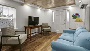 Una sala de estar moderna con techo de madera, televisor de pantalla plana, sofá azul, dos sillones y una pequeña mesa.