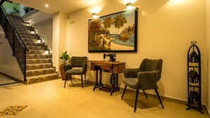 A staircase leading to a higher floor, a painting of a tropical scene, a sewing machine, and two chairs in a well-lit room.