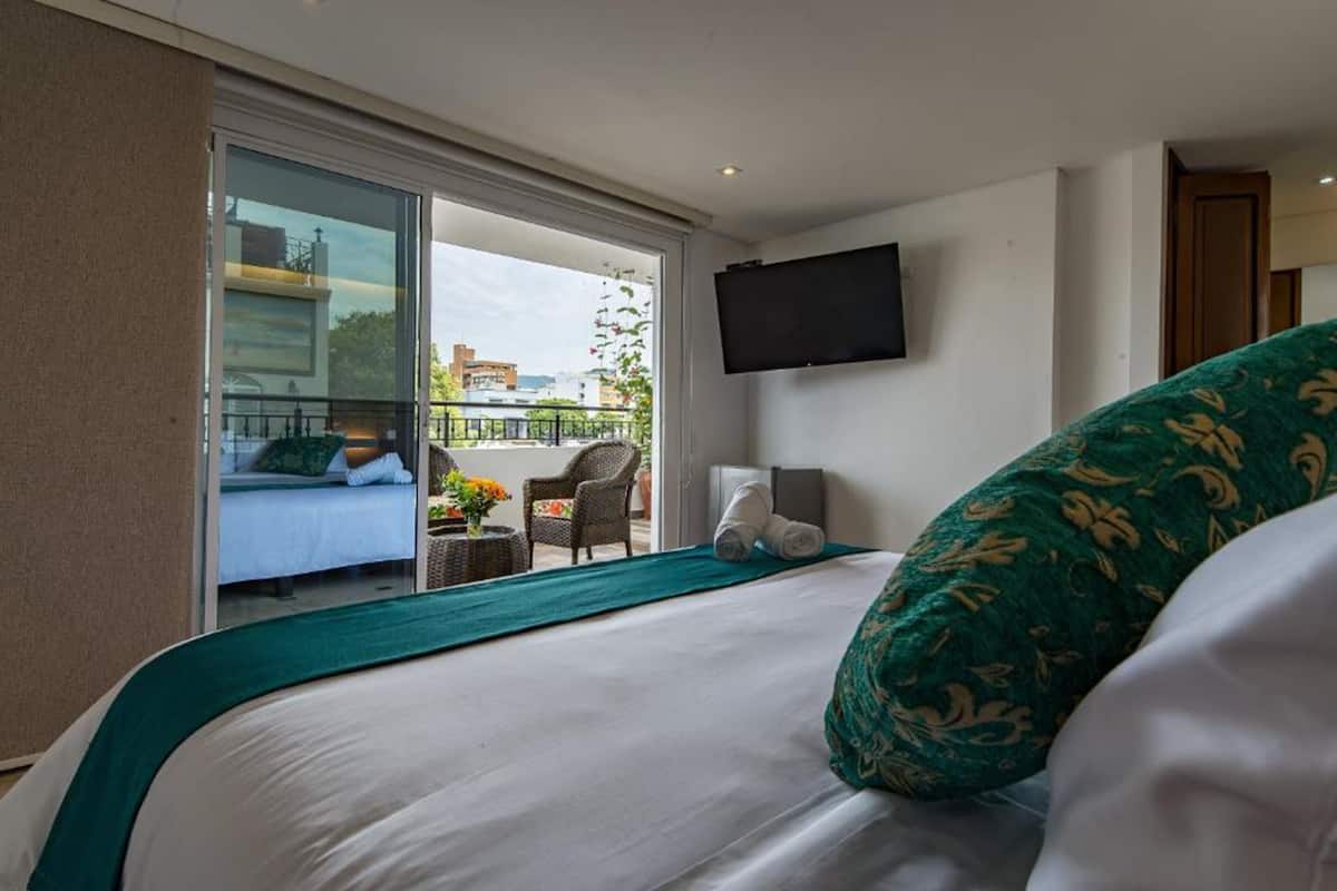 A hotel room with a bed, a TV mounted on the wall, and a balcony with a view of the city.