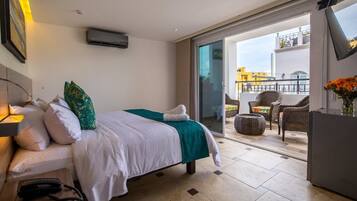 A hotel room with a bed, a telephone, a window, and a balcony with wicker furniture.