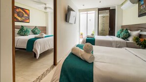 A hotel room with two beds, each with a teal bedspread and white linens. There is a ceiling fan, a flat-screen TV mounted on the wall, and a door leading to a balcony.