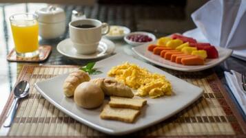 A breakfast plate with eggs, croissants, and toast, a glass of orange juice, a cup of coffee, and a plate of fruit on a table.
