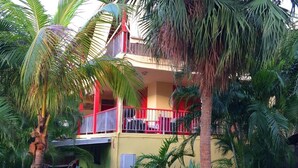A two-story building with a balcony, surrounded by dense tropical foliage. - Gite T4 MONTANA 200 m2, 7/9 beds, 2 bathrooms and 2 separate toilets, 350 m beach. (Deshaies)