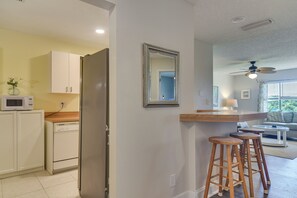 Eine Küche mit weißen Schränken, einer Mikrowelle und einem Kühlschrank. Es gibt eine Holzbar mit Hockern und einen Deckenventilator.