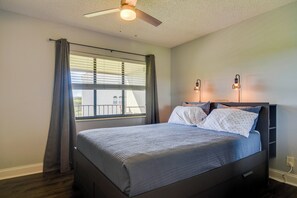 Ein Schlafzimmer mit einem Bett, einem Deckenventilator, einem Fenster mit Vorhängen und zwei Wandleuchten.