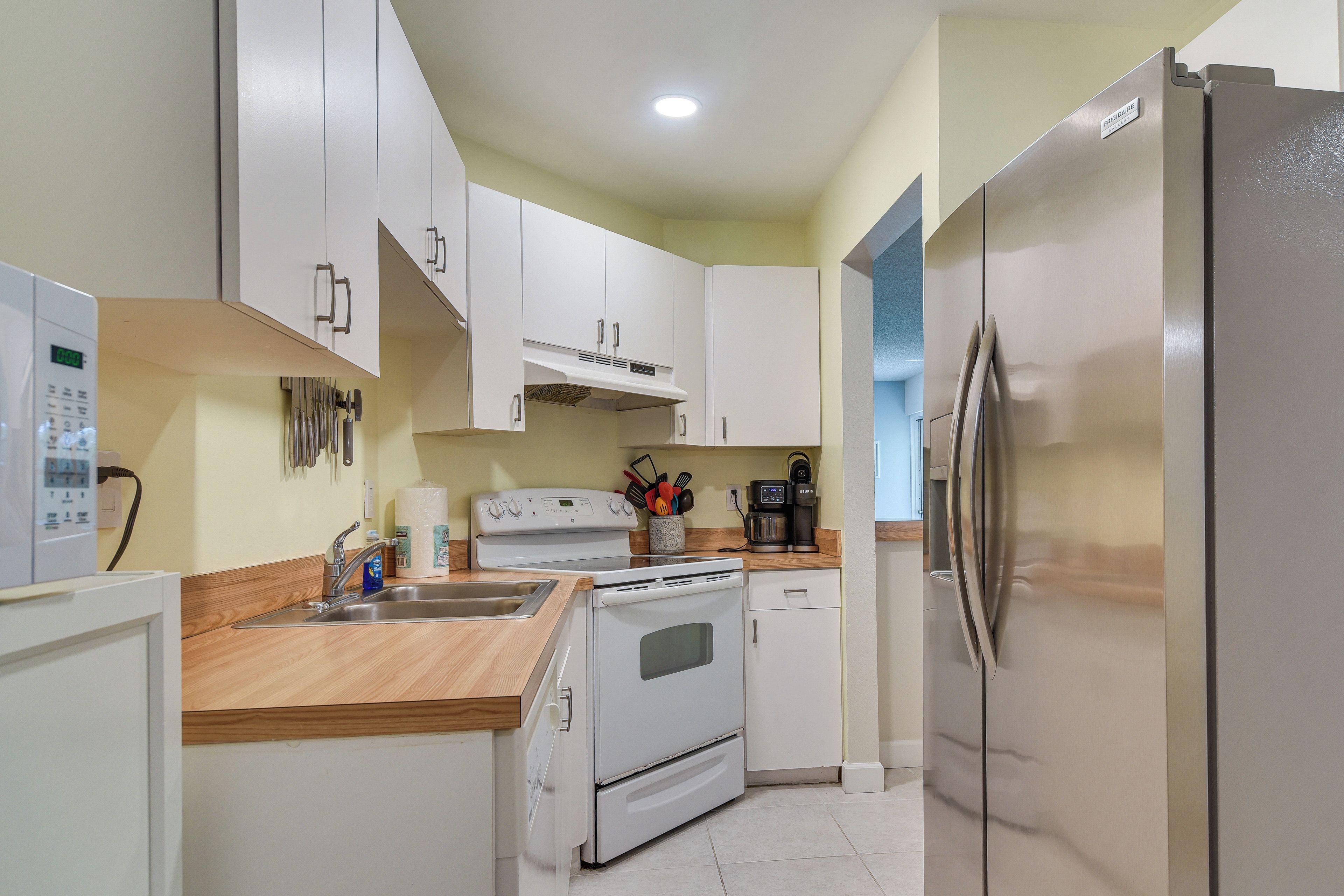 Una cocina compacta con armarios blancos, un refrigerador de acero inoxidable, horno empotrado y cafetera.