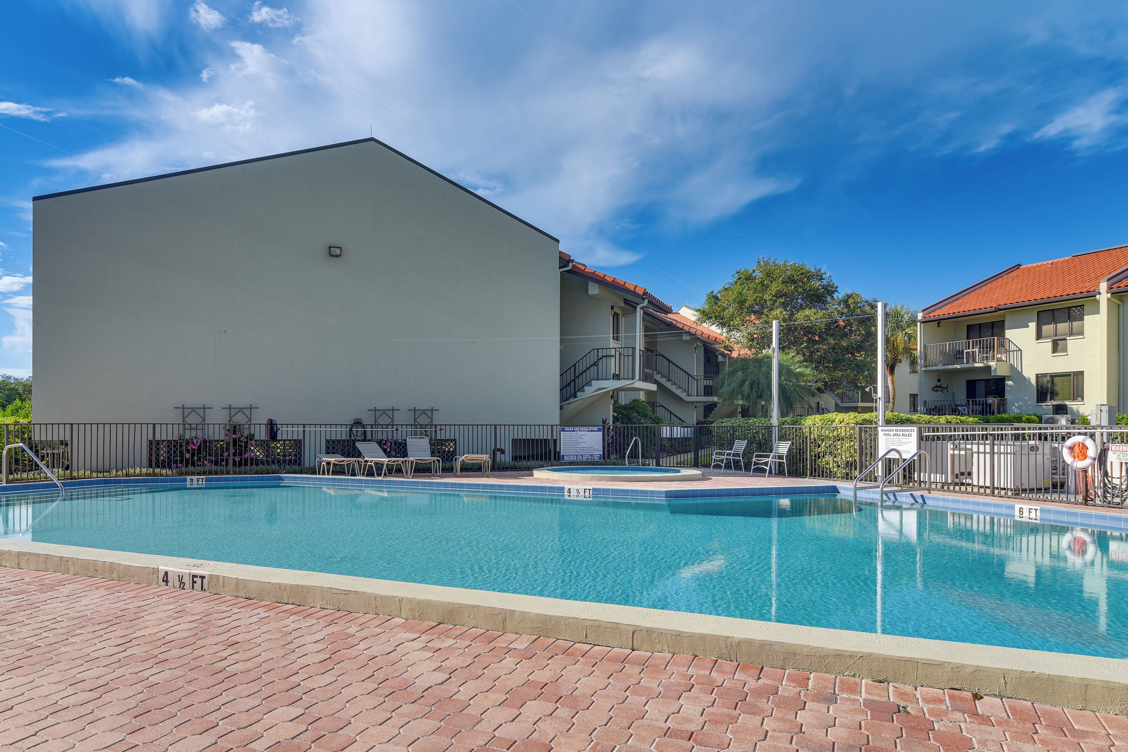 A swimming pool with a brick deck, adjacent to a building with a flat roof and a balcony.