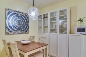 Ein Essbereich mit Holztisch, Stühlen, einer Glaskandelier, einem Schrank mit Glastüren und einem an der Wand hängenden Kunstwerk.