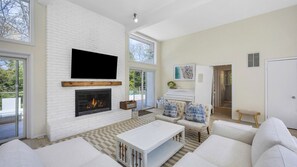 A modern living room with a fireplace, white sofas, a flat-screen TV, and a piano.