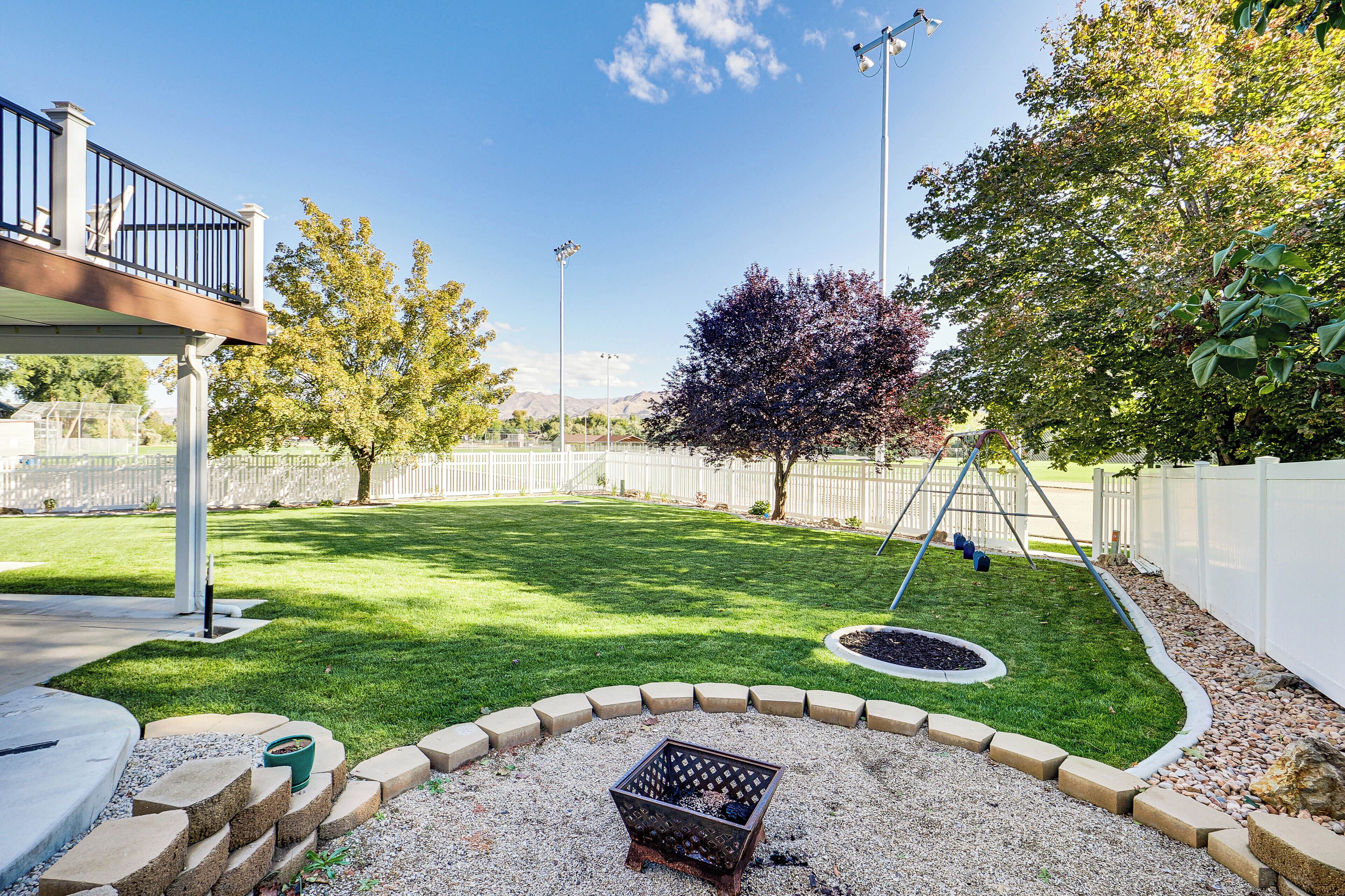 A well-maintained backyard with a lawn, a fire pit, a swing set, and a wooden deck.
